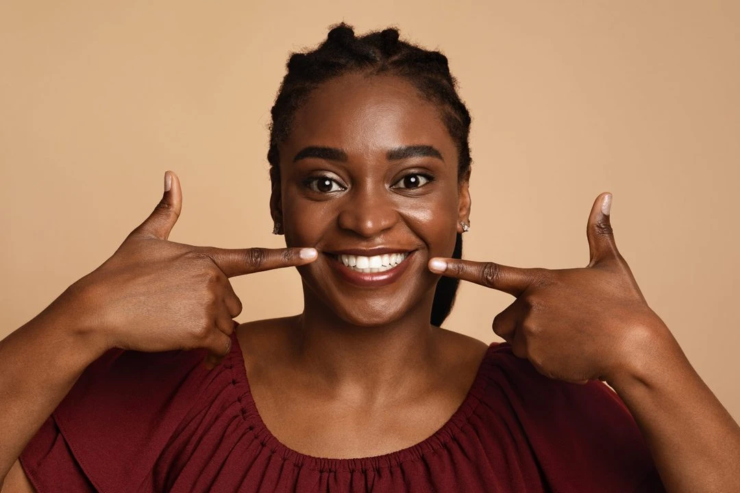Positive black woman showing her beautiful white teeth A glass entrance door for Pinecrest Family Dental featuring office hours, the name of Dr. Taidy Costoya, DMD, and the phone number (305) 235-0020.